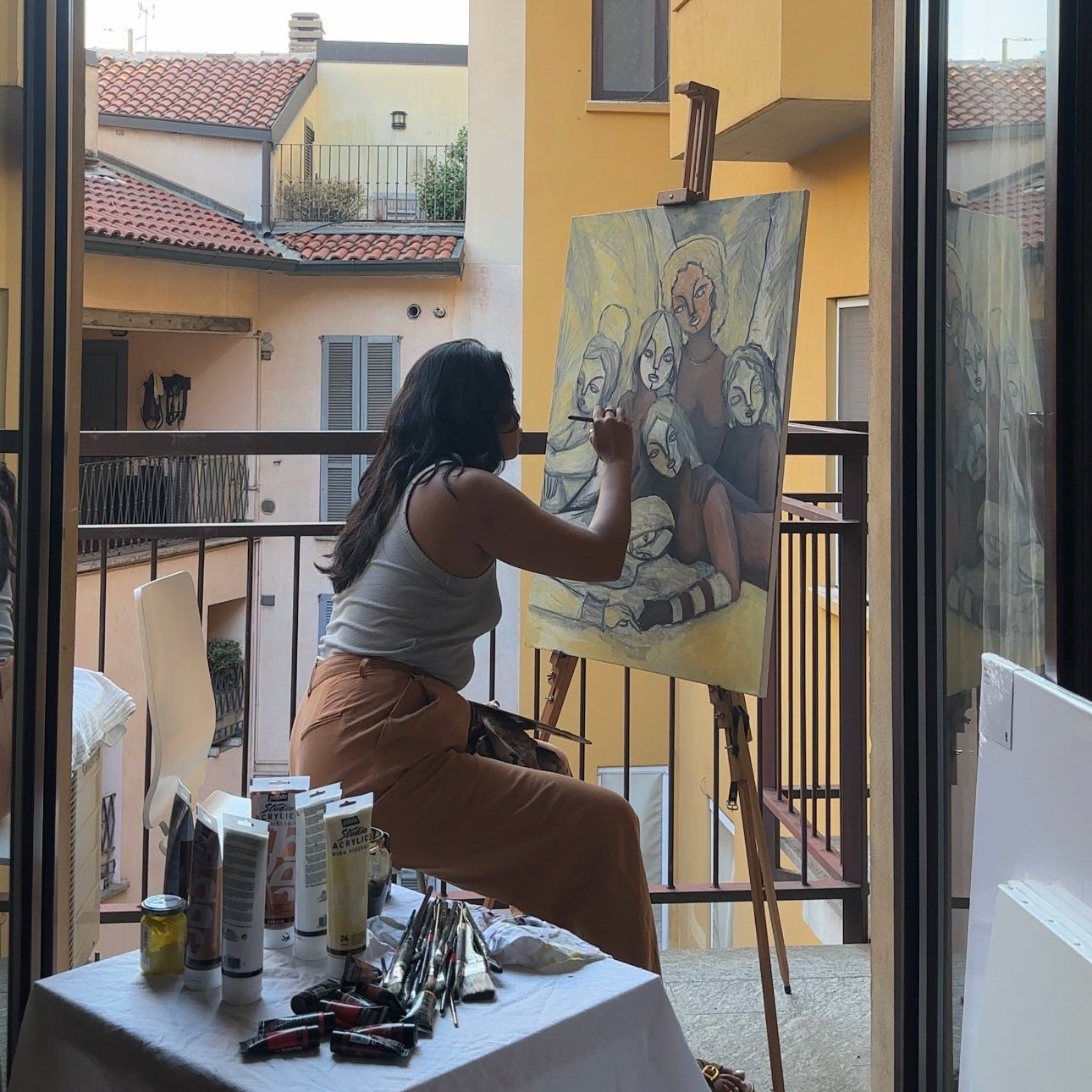 Person painting outdoors on a balcony with a view of buildings.